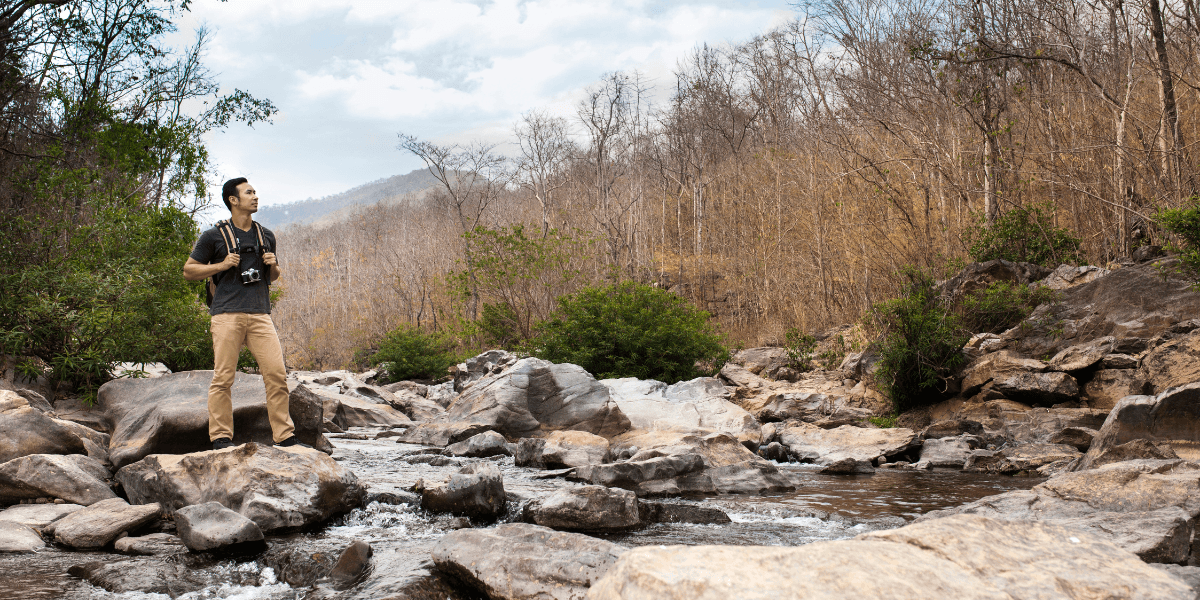 A man stands on rocks in a flowing river, surrounded by nature and water splashing around him.