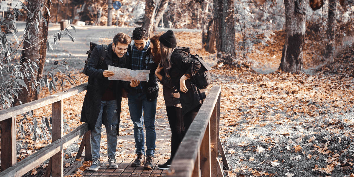 Three individuals studying a map while surrounded by trees in a wooded area.