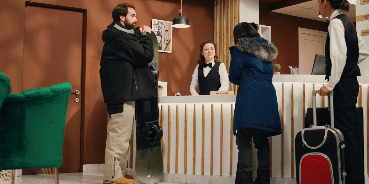 A man and woman stand at a hotel reception desk, engaging with the receptionist for check-in assistance.