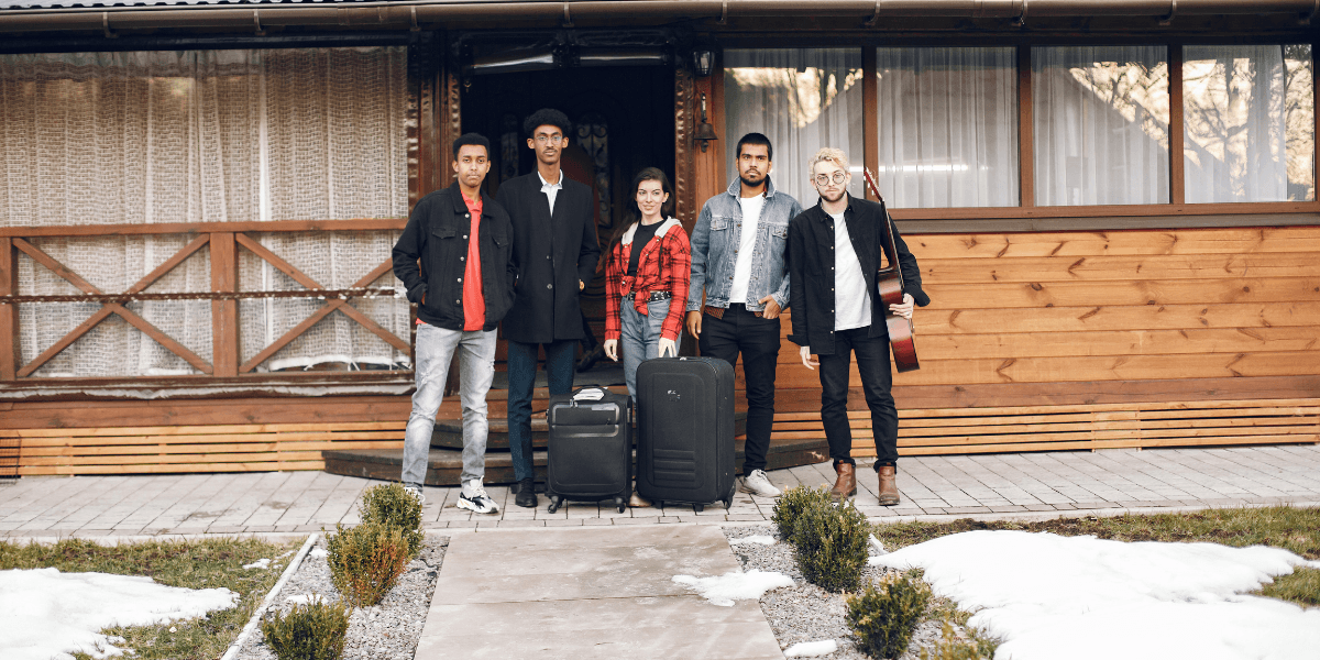 A group of five people stands outside a house, each holding luggage, ready for a trip or vacation.