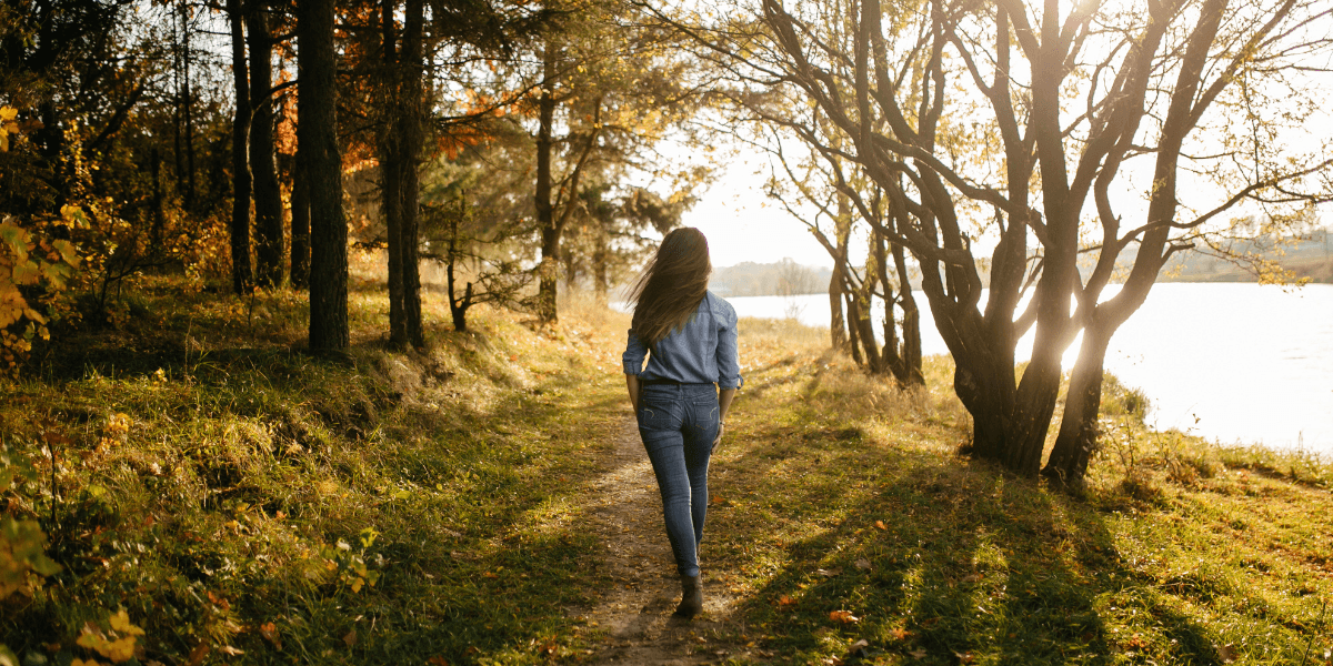A woman strolls along a lakeside path, surrounded by greenery and reflecting water.